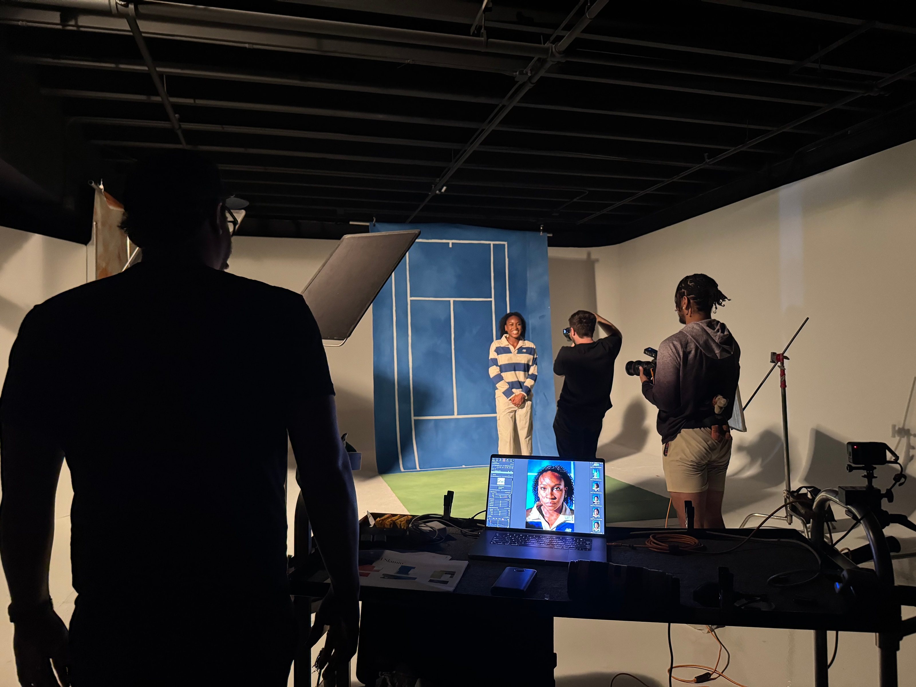 The crew shoots Coco Gauff in front of painted court backdrops, a laptop tethered on set