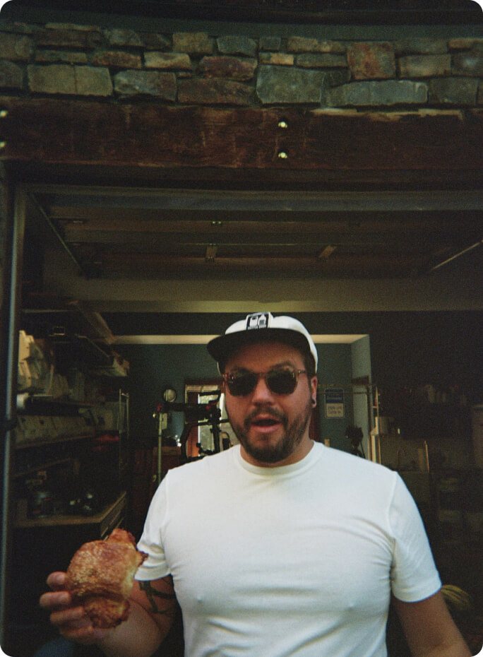 A crew member in sunglasses holding a pastry outside the garage set
