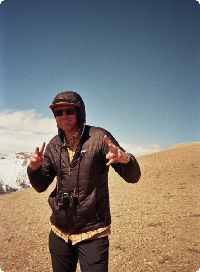 A crew member with a film camera around his neck on a high ridge
