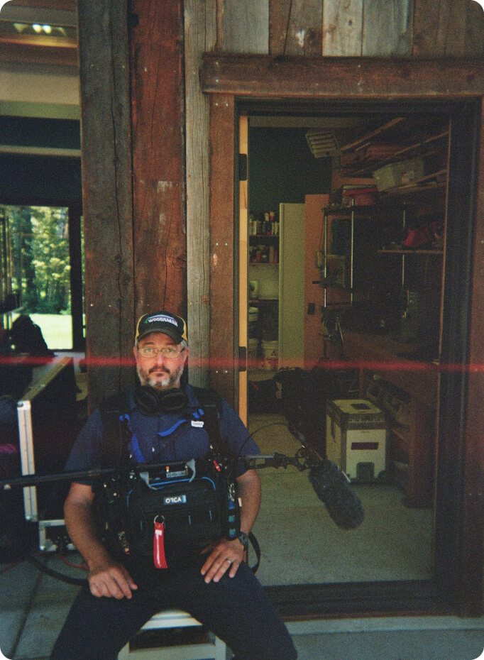 The sound mixer sitting in a doorway with his recorder and boom mic