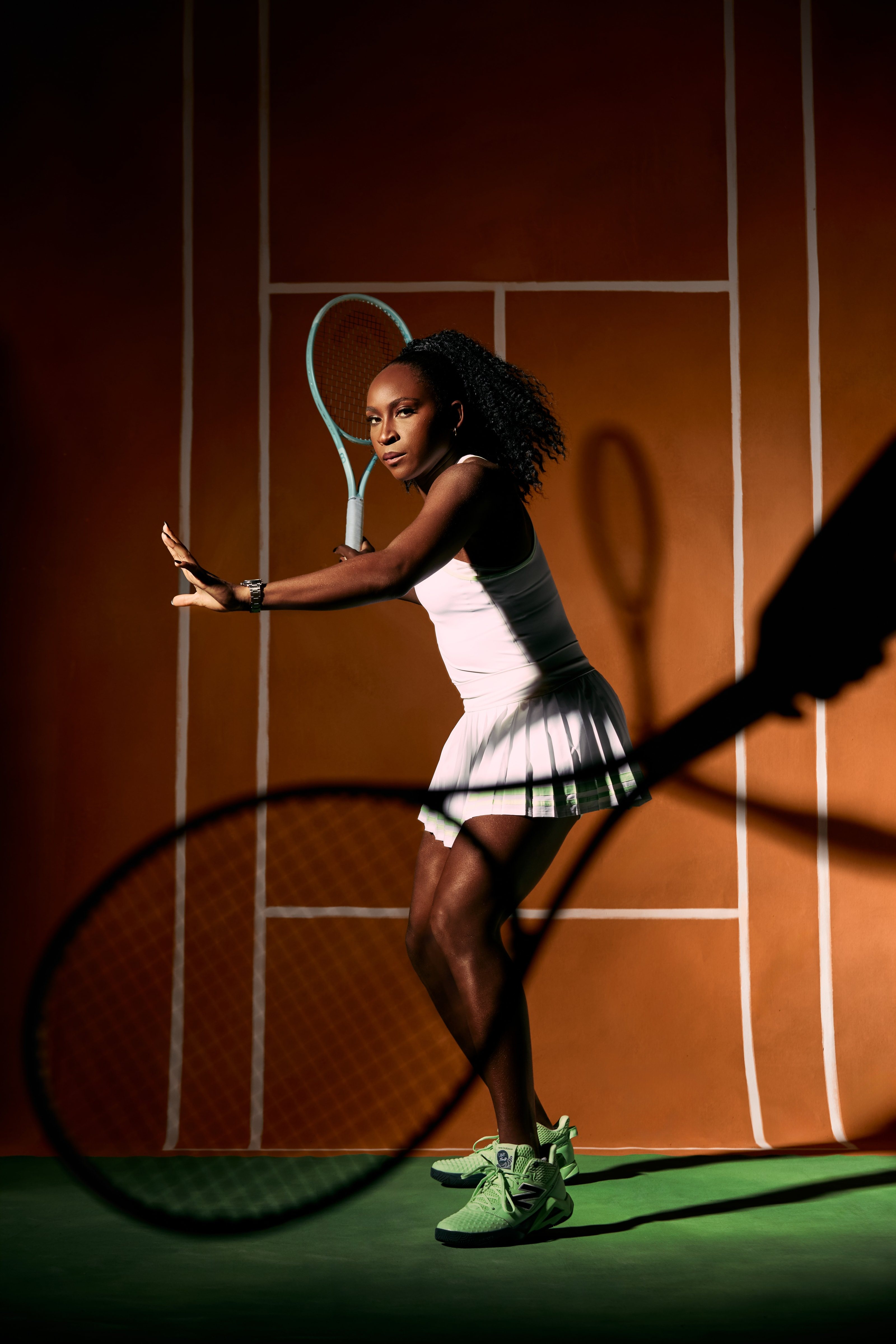 Coco Gauff holds her racquet back on a painted clay court with its shadow across the frame