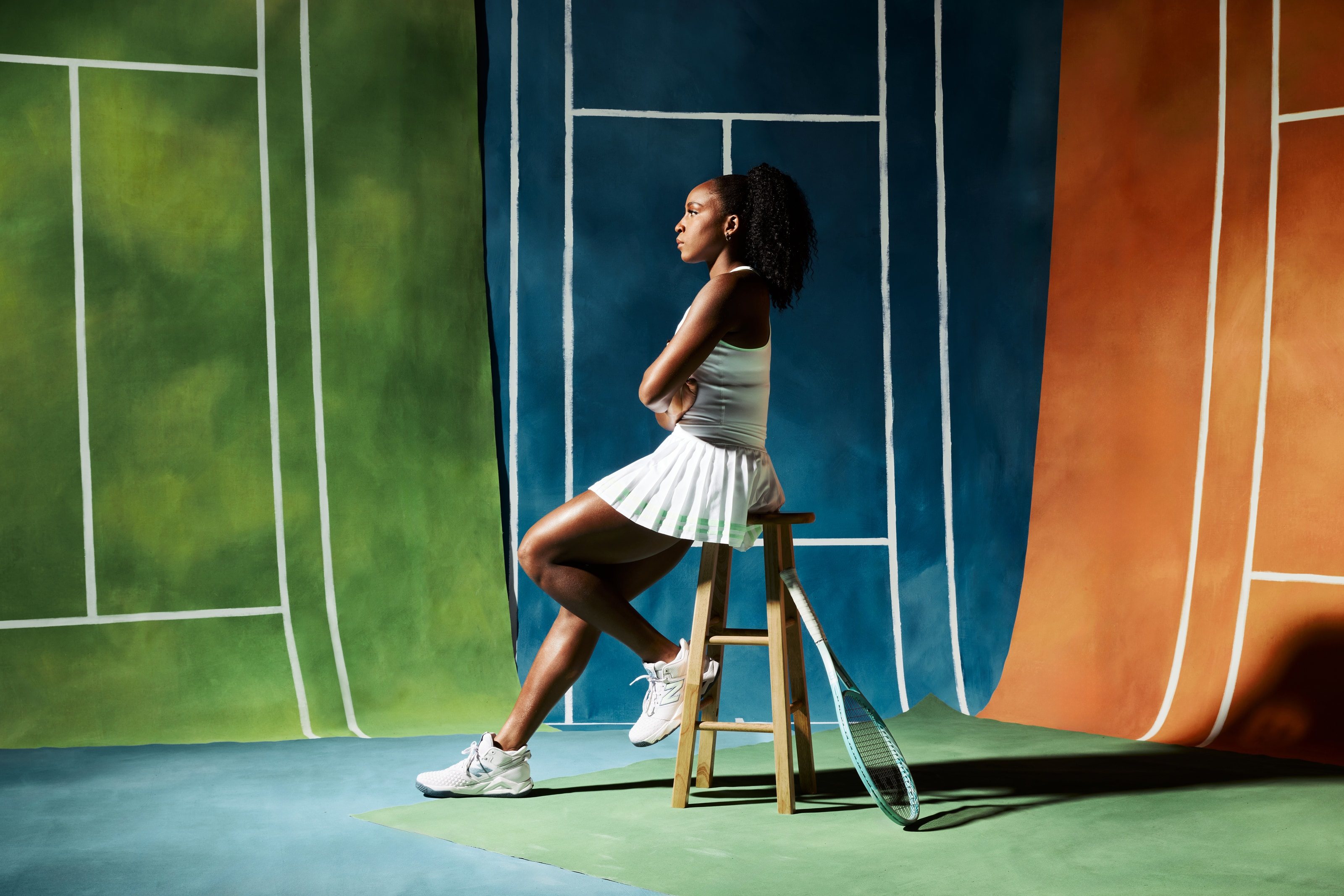Coco Gauff sits on a stool with her racquet against painted court backdrops