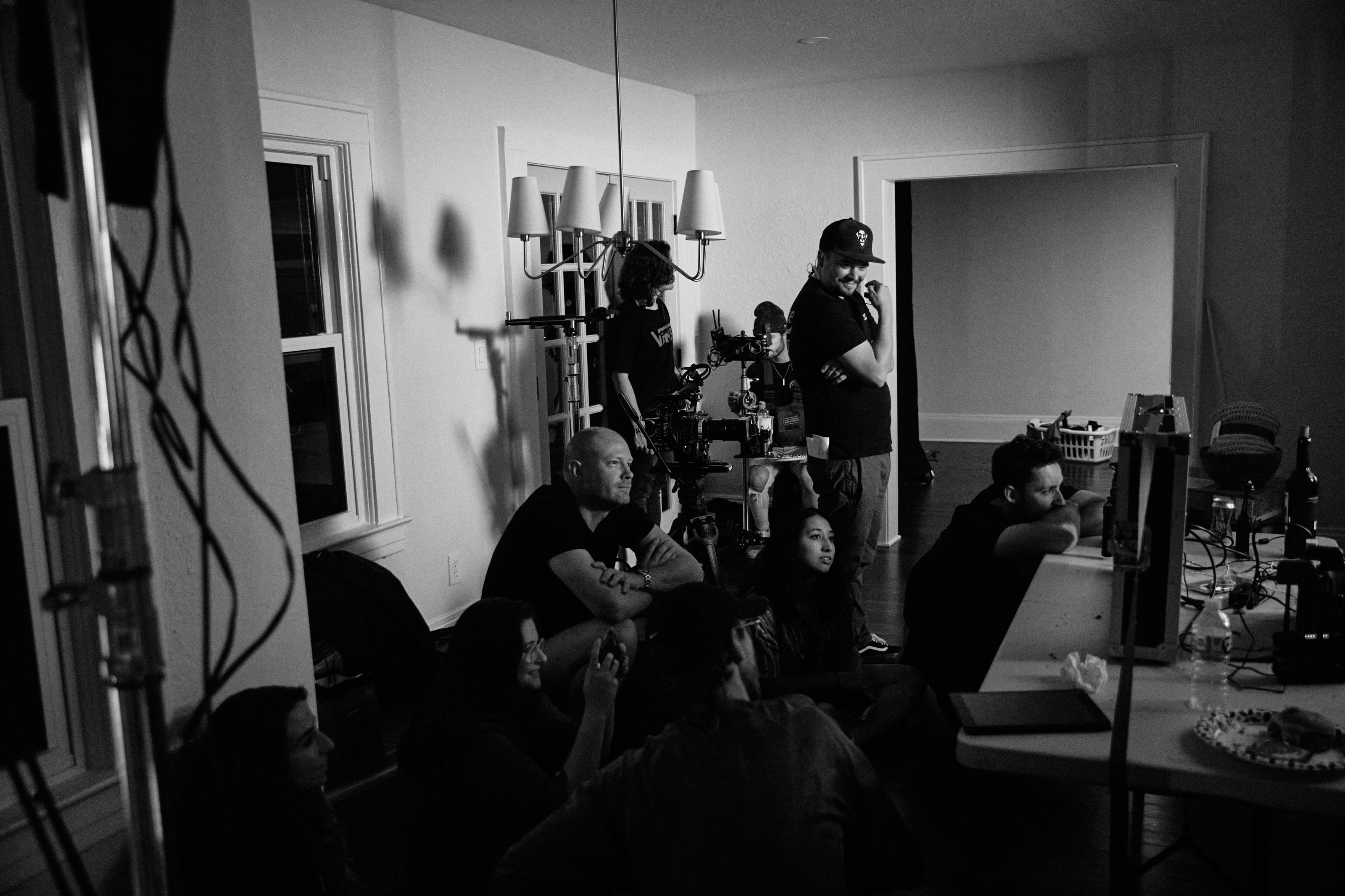 The crew gathered around the monitors in a house on a shoot, in black and white