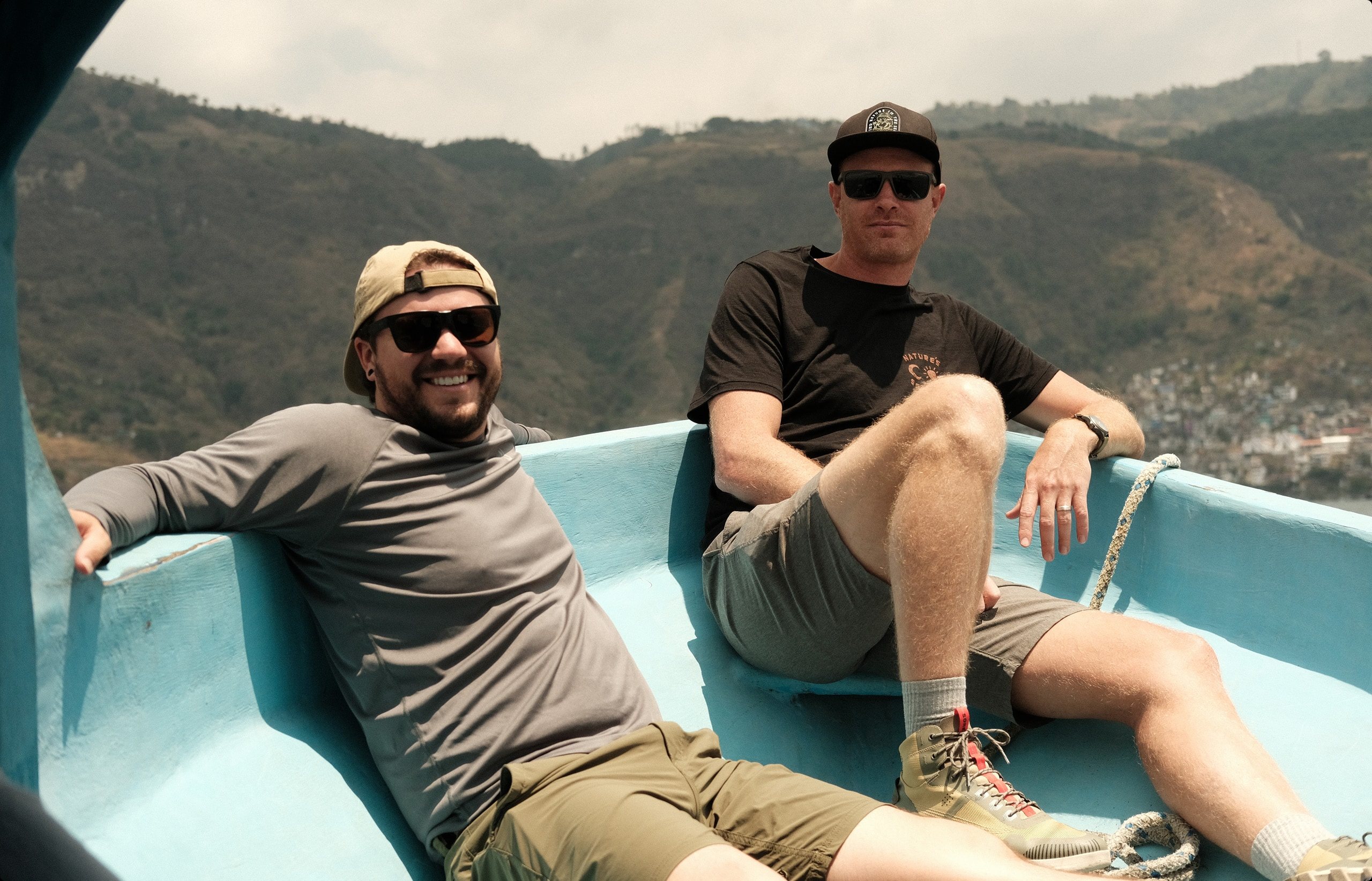 Josh and Derek kicking back in a small turquoise boat above a mountain lake