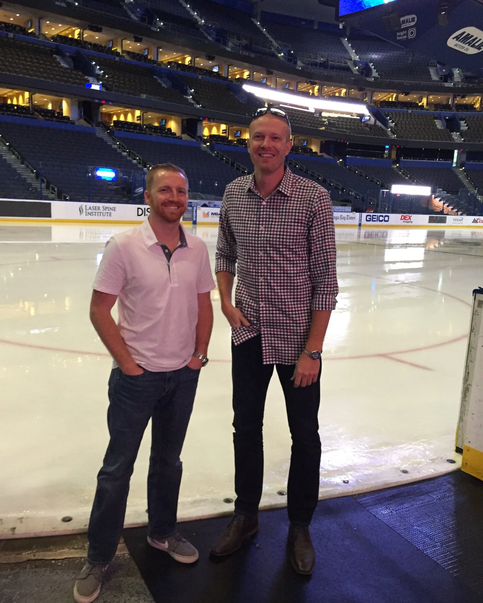 Derek and Chris standing on the floor of an empty hockey arena