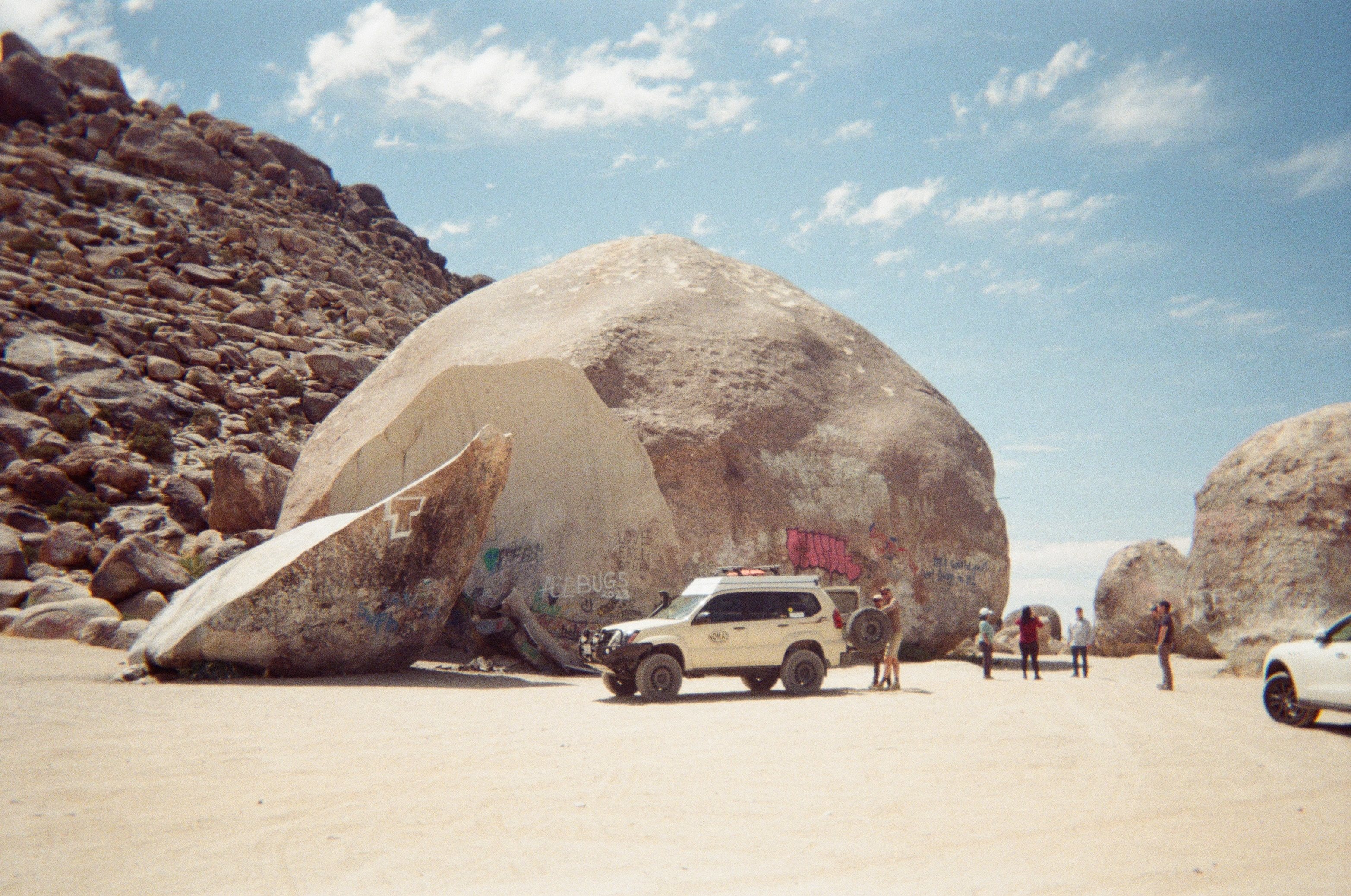 A 4x4 and a small crew beside a giant split boulder in the desert