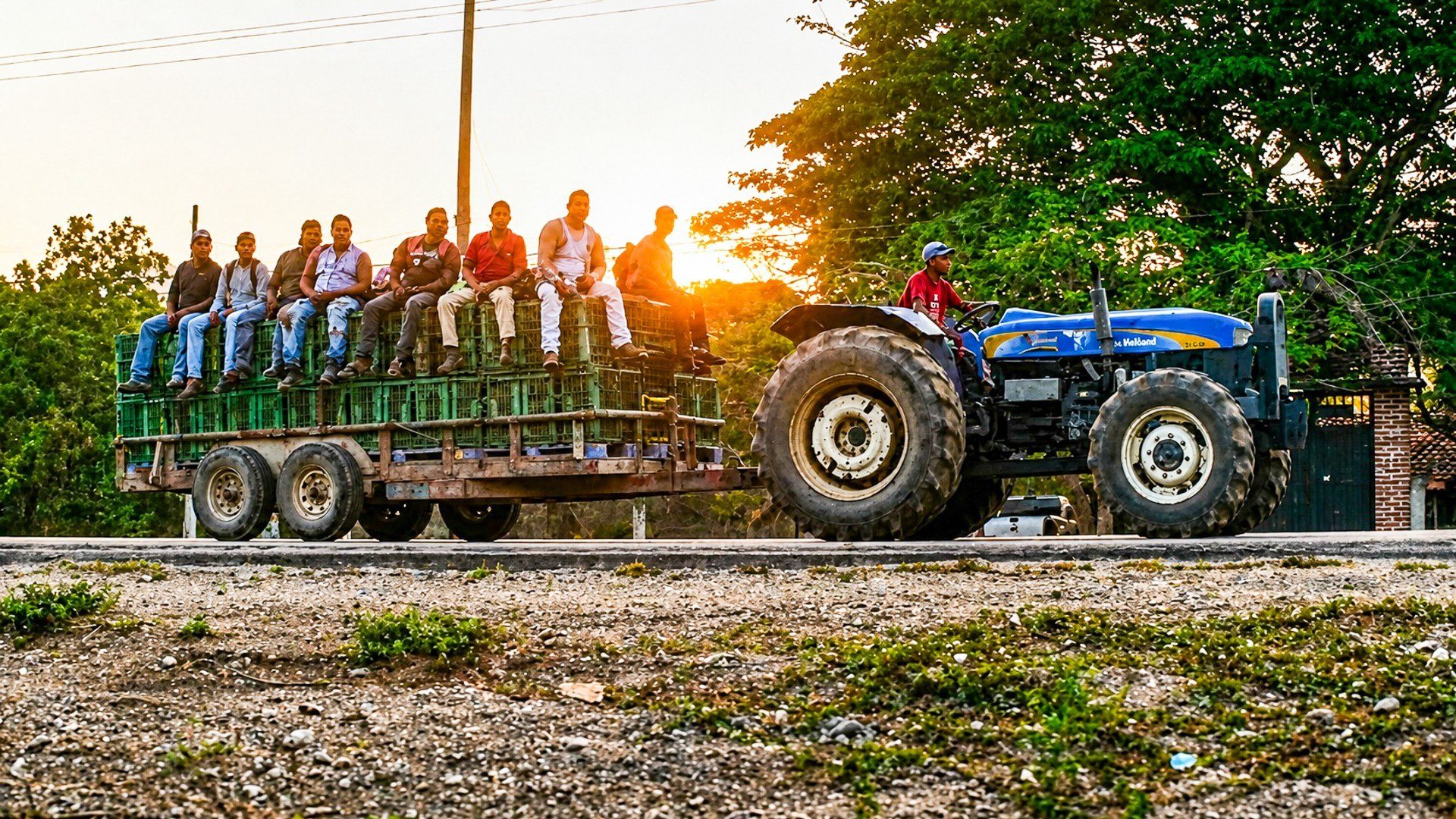 Workers ride a trailer behind a tractor at golden hour