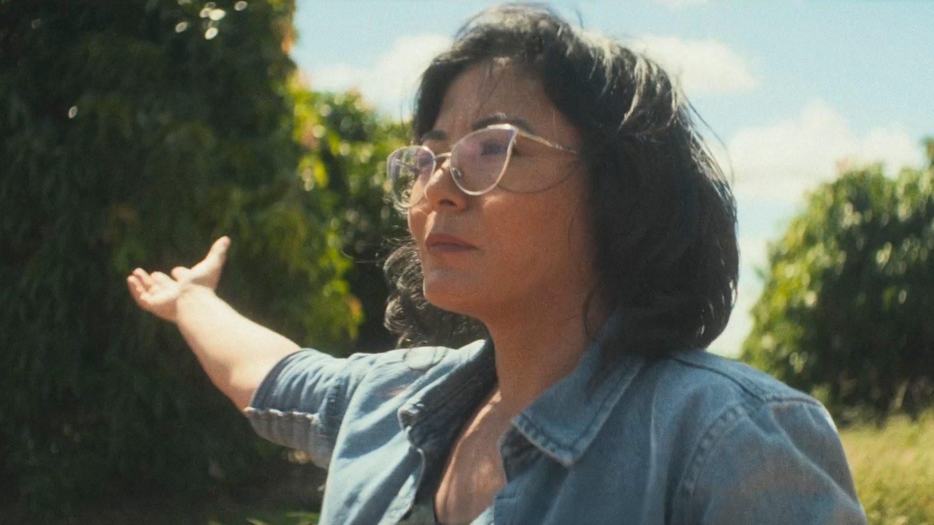 A woman in glasses gestures across an orchard