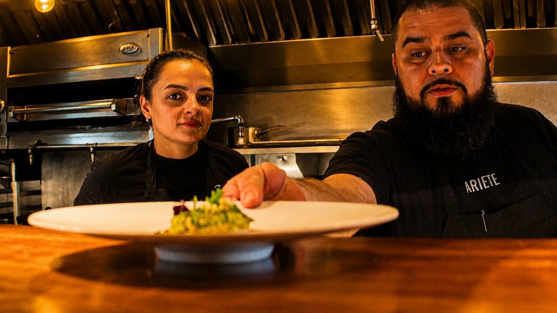 Two chefs present a plated dish across a restaurant pass