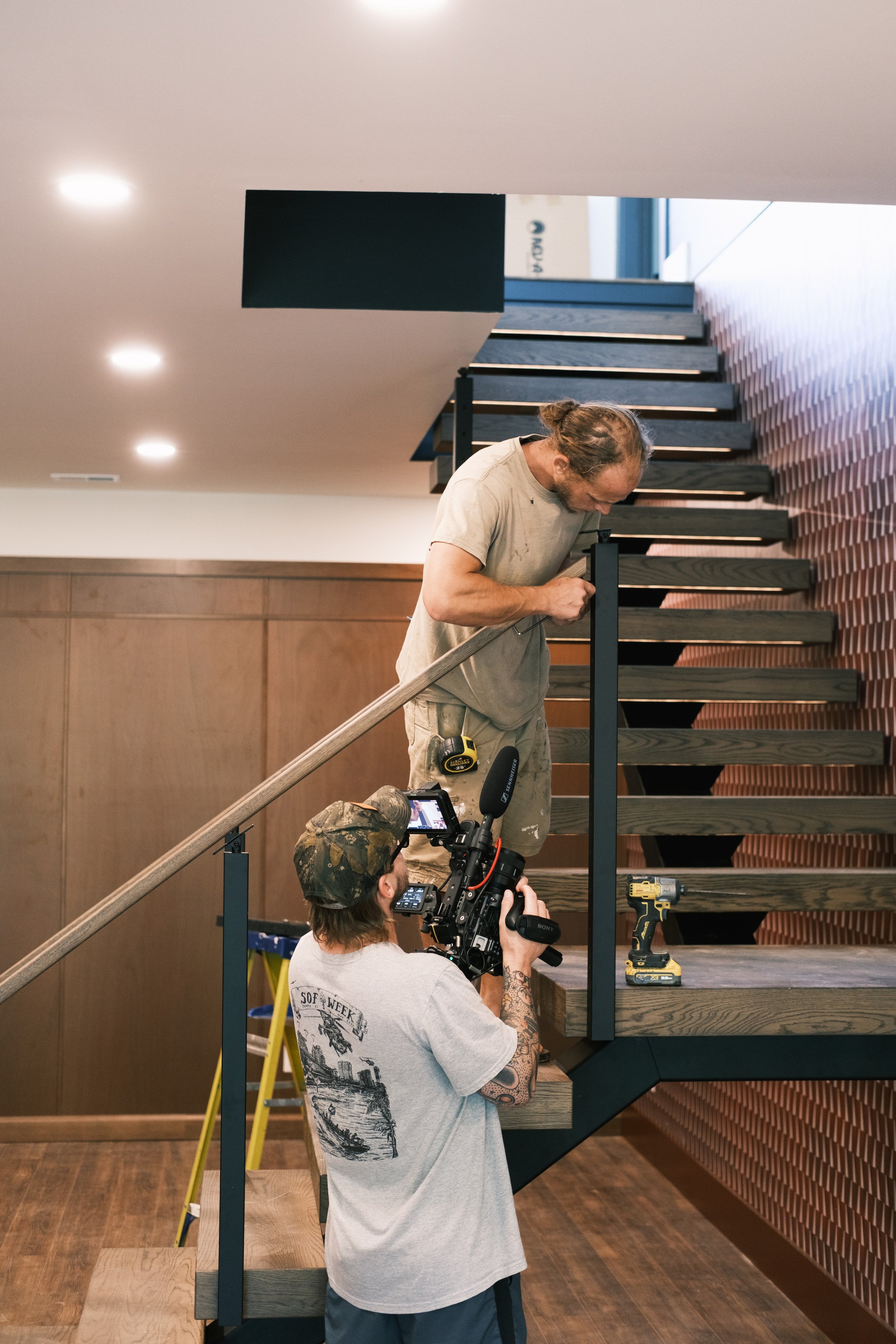 A camera operator filming a builder at work on the staircase inside the Smith Lake house