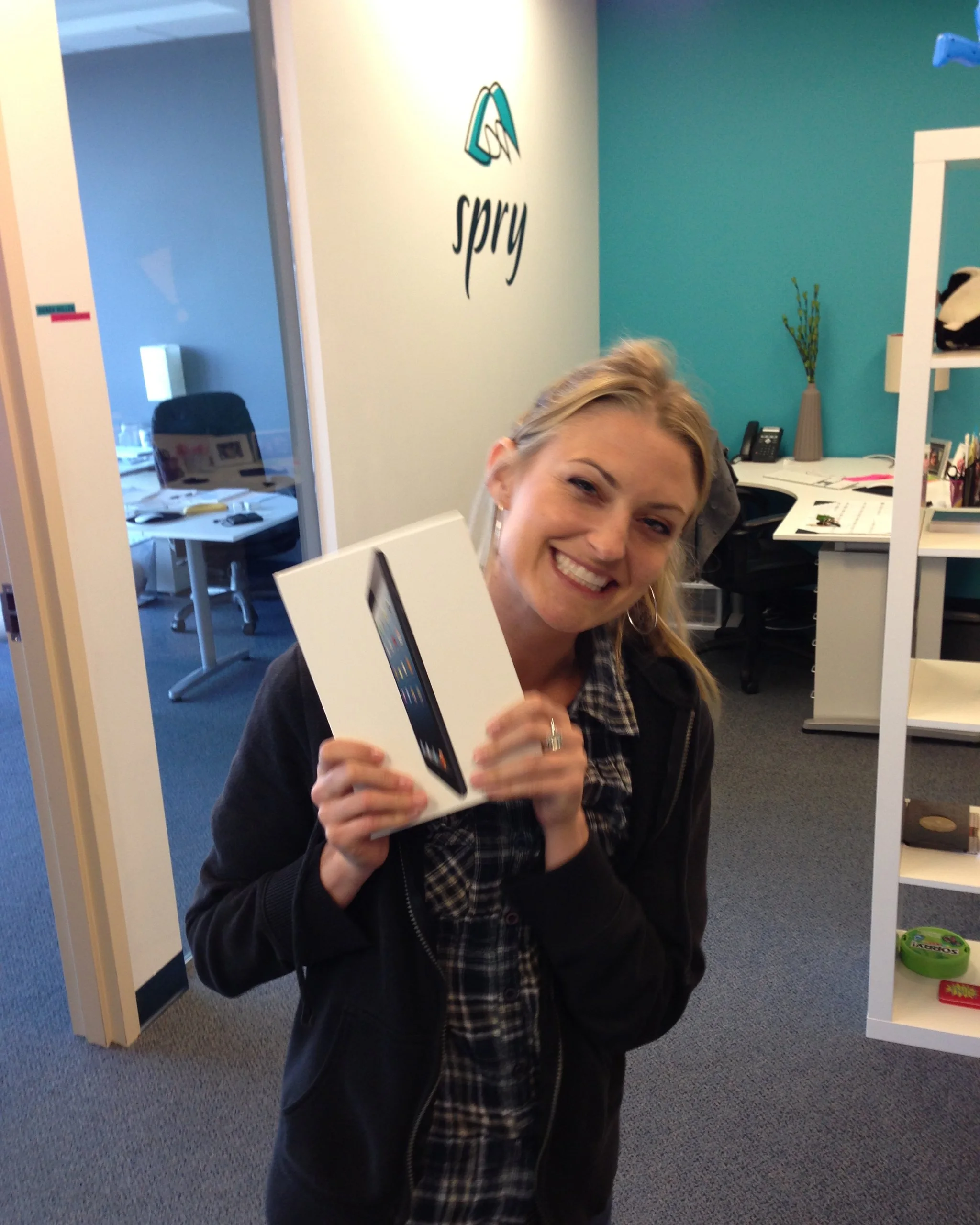 Alison grinning and holding up a new iPad box in front of the Spry logo