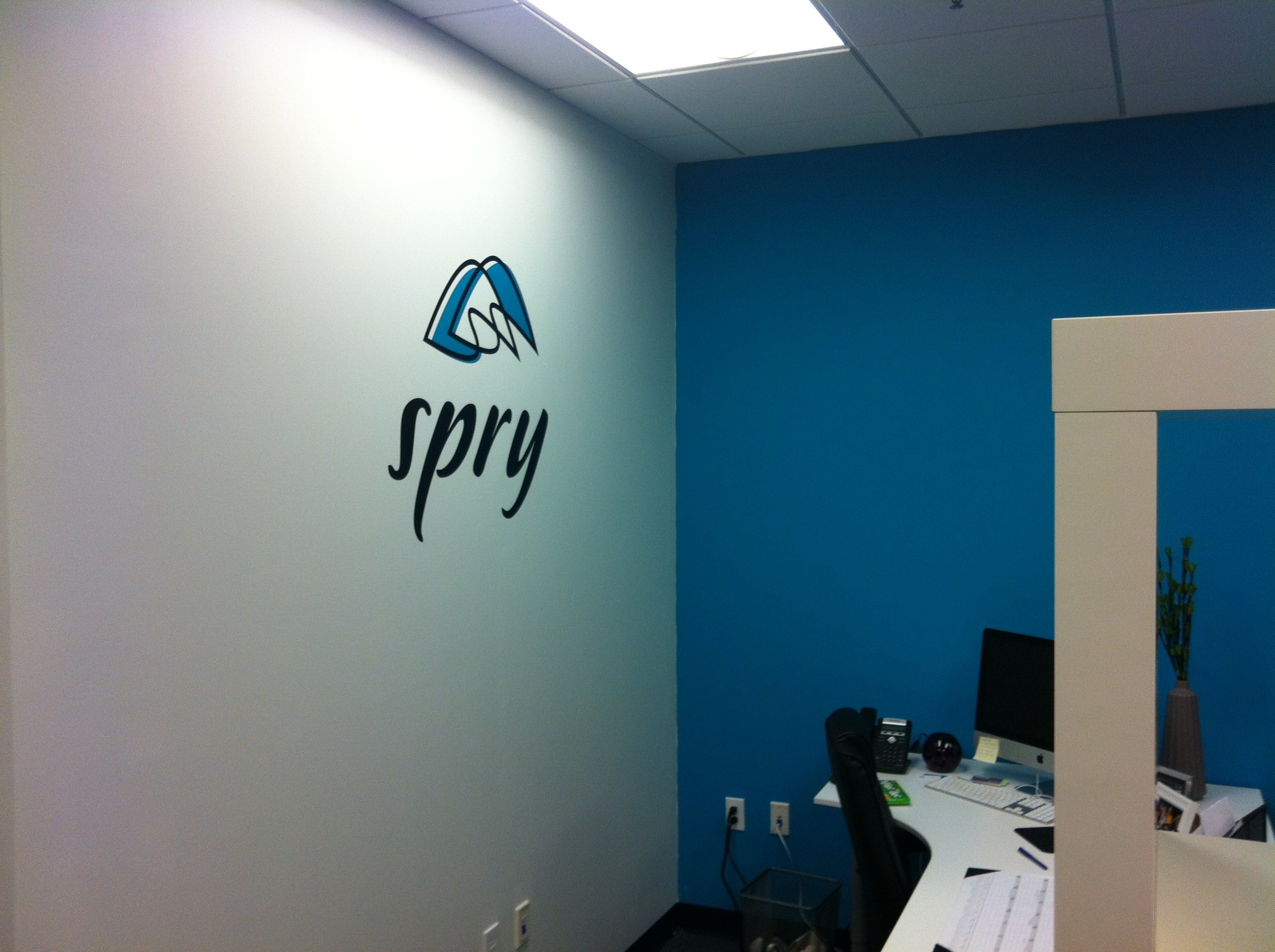 The old Spry logo on a white wall beside a bright blue accent wall in Spry's first office