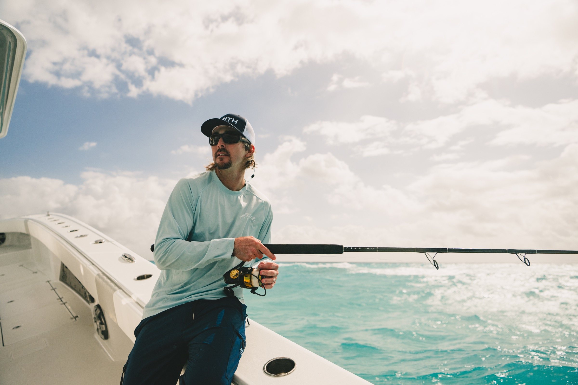 A guide works a rod and reel at the stern under a bright sky