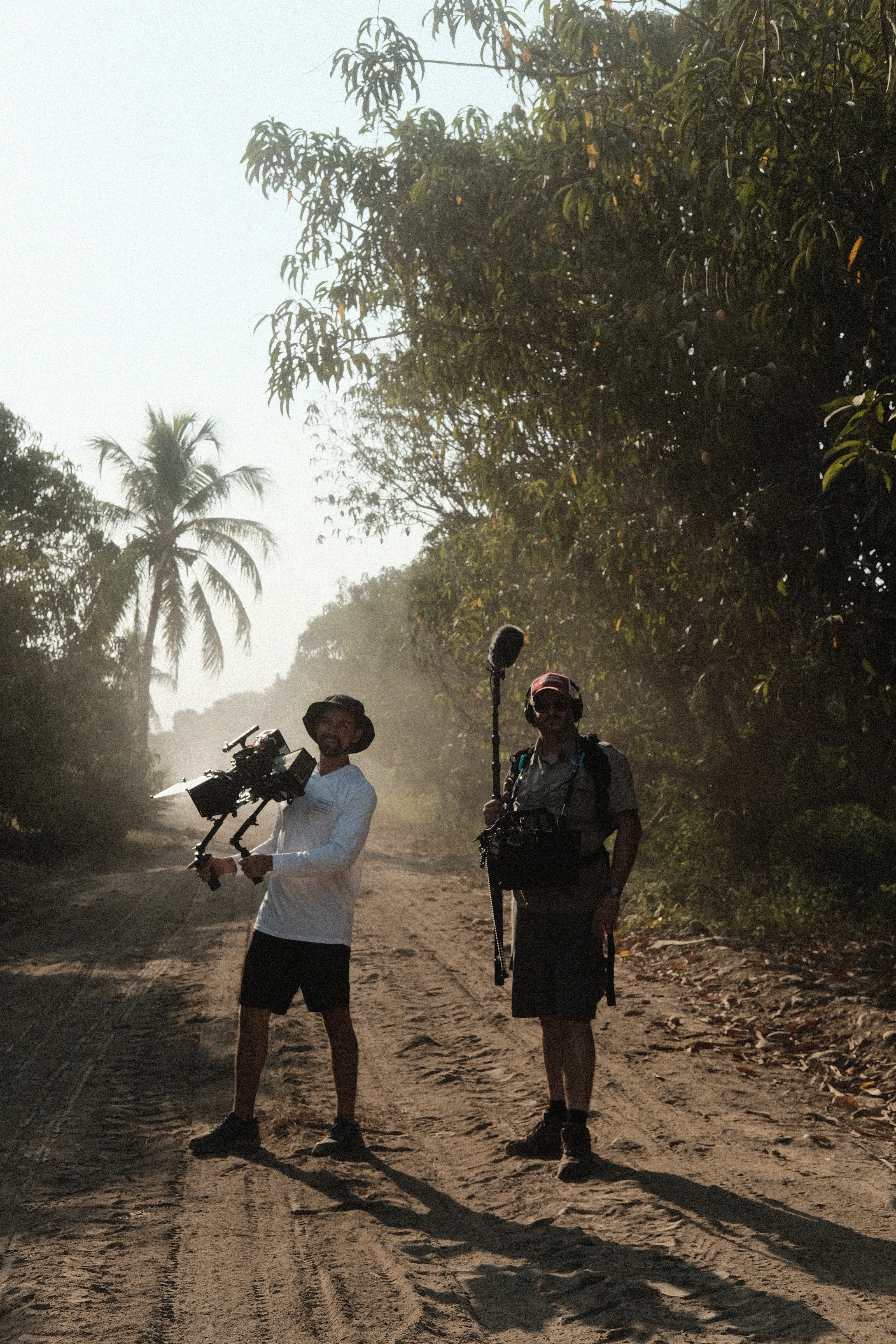 A camera operator and a sound recordist at work on a dusty road under the palms