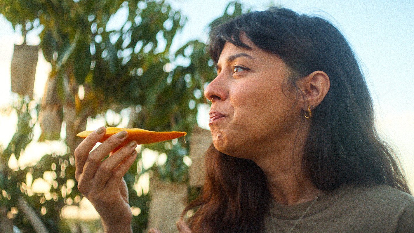 A woman takes a bite of fresh mango in an orchard