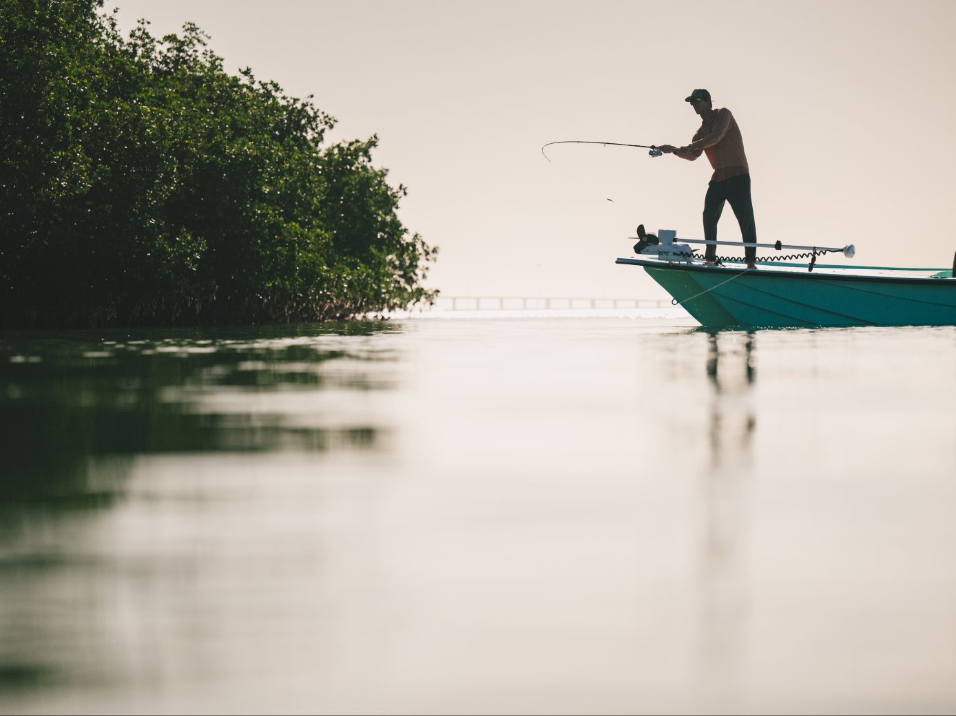 An angler stands on the bow of a skiff casting beside the mangroves