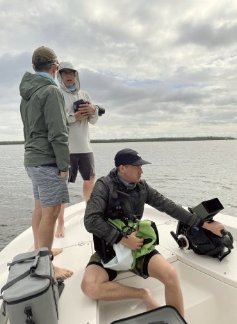 Three crew members on the bow of a boat under a cloudy sky