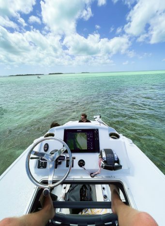 A view from the helm of a boat over the steering wheel and console, turquoise shallows ahead