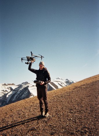 A drone operator holding the drone overhead on a mountain slope