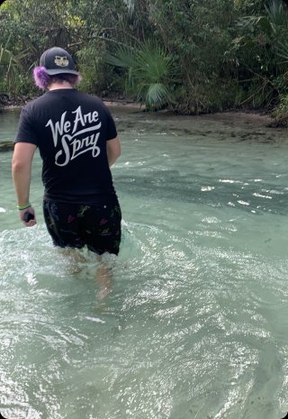 A crew member in a We Are Spry shirt wades through a clear spring