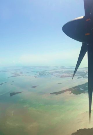 A propeller plane's wing over shallow flats and islands seen from the air