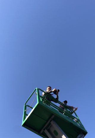 Two people on a green lift high against a blue sky
