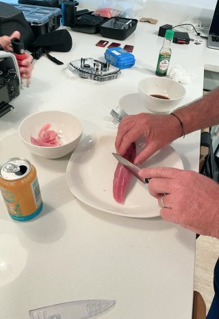 Someone slices a strip of raw fish on a plate at a kitchen counter