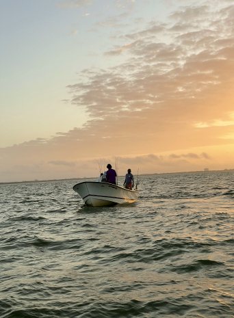 Two people standing on a small boat on open water at sunset