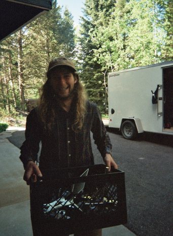 A smiling crew member carrying a crate of gear past the trailer