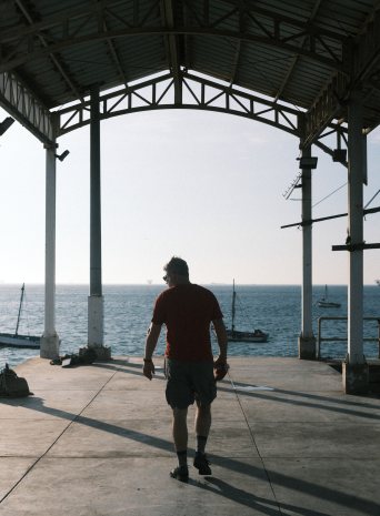 A man walks toward the sea under an open pier shelter