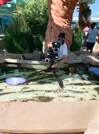 A camera operator in a mask films low over a shallow touch pool