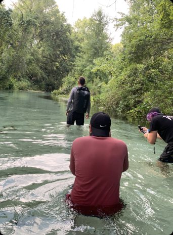 The crew wades waist-deep in a spring behind a man wearing a dry bag