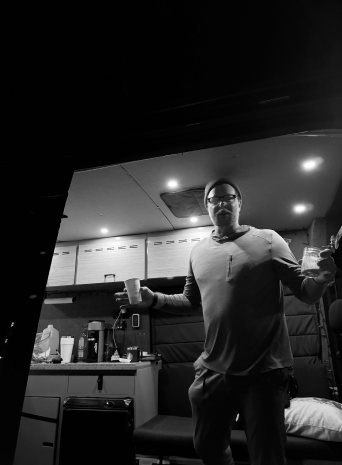 A man raises a cup inside a camper kitchen at night