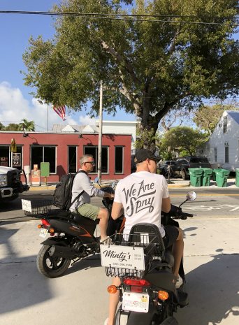 Two crew members on scooters at a street corner in town