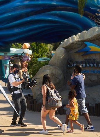 A camera operator films a family walking toward the SeaWorld San Diego sign
