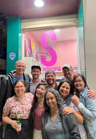 The crew and a group of women pose outside a bright pink shop at night