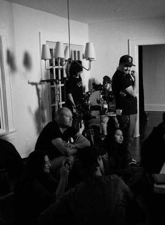 Black and white photo of the crew gathered around the camera in a living room