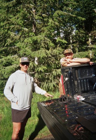 Two crew members by the tailgate of a truck in the trees
