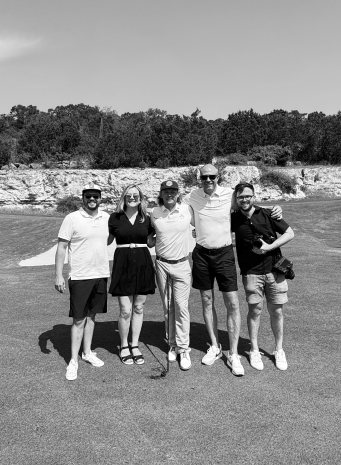Five people pose arm in arm on a golf course