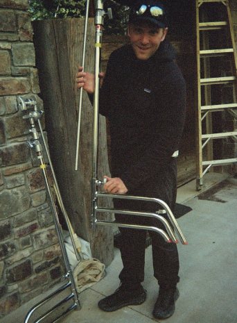 A grip carrying light stands past a stone wall