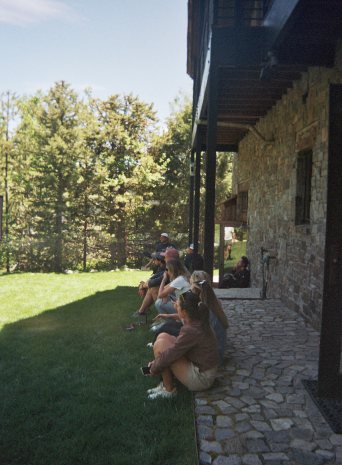 People sitting in the shade along the house wall on the lawn