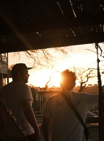 Two crew members silhouetted against the setting sun under a porch roof