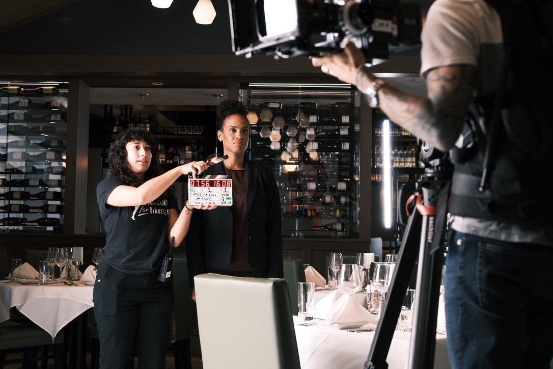 A camera assistant slates a take with an actor in the restaurant dining room