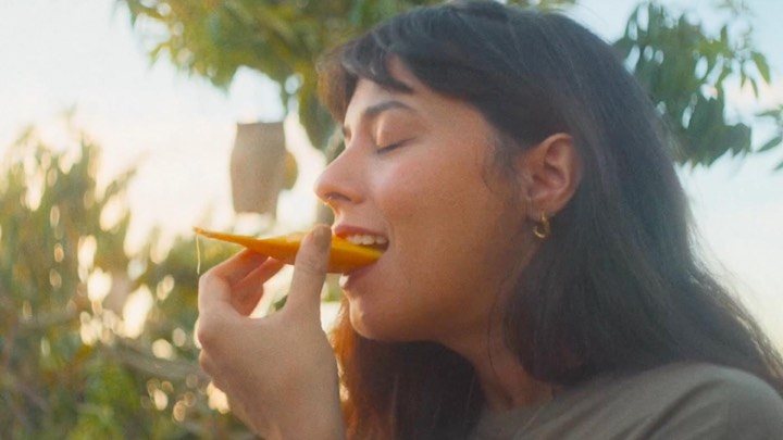 A woman closes her eyes as she bites into a slice of mango