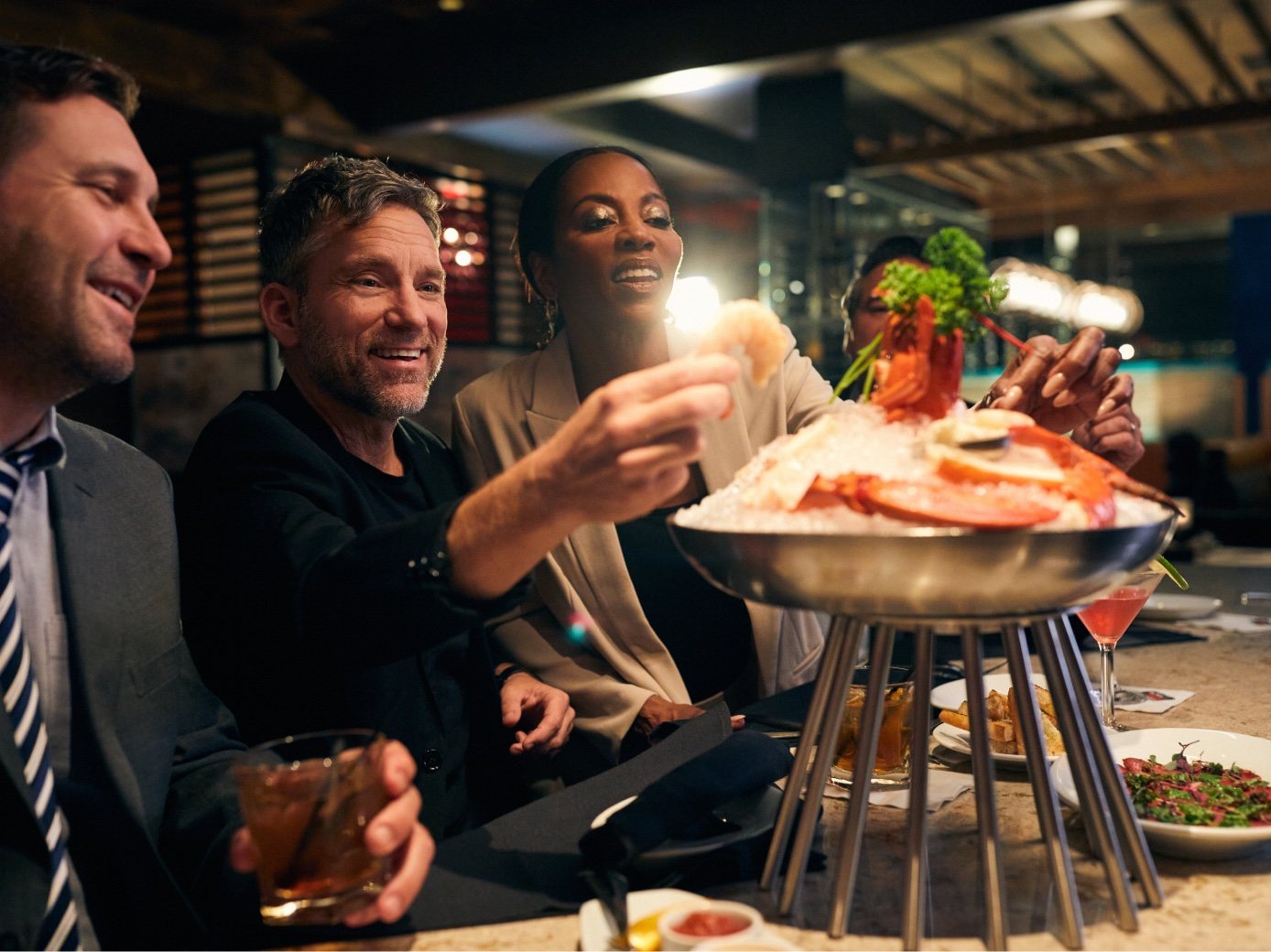 Friends at the bar laugh and reach for a seafood tower
