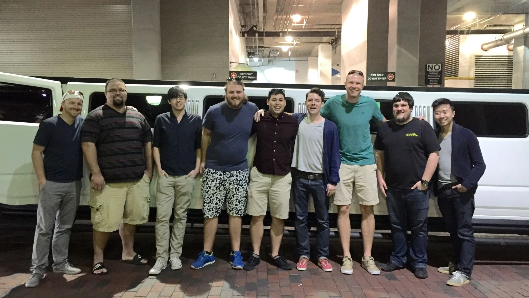 Nine of the team lined up in front of a white stretch limo in a parking garage