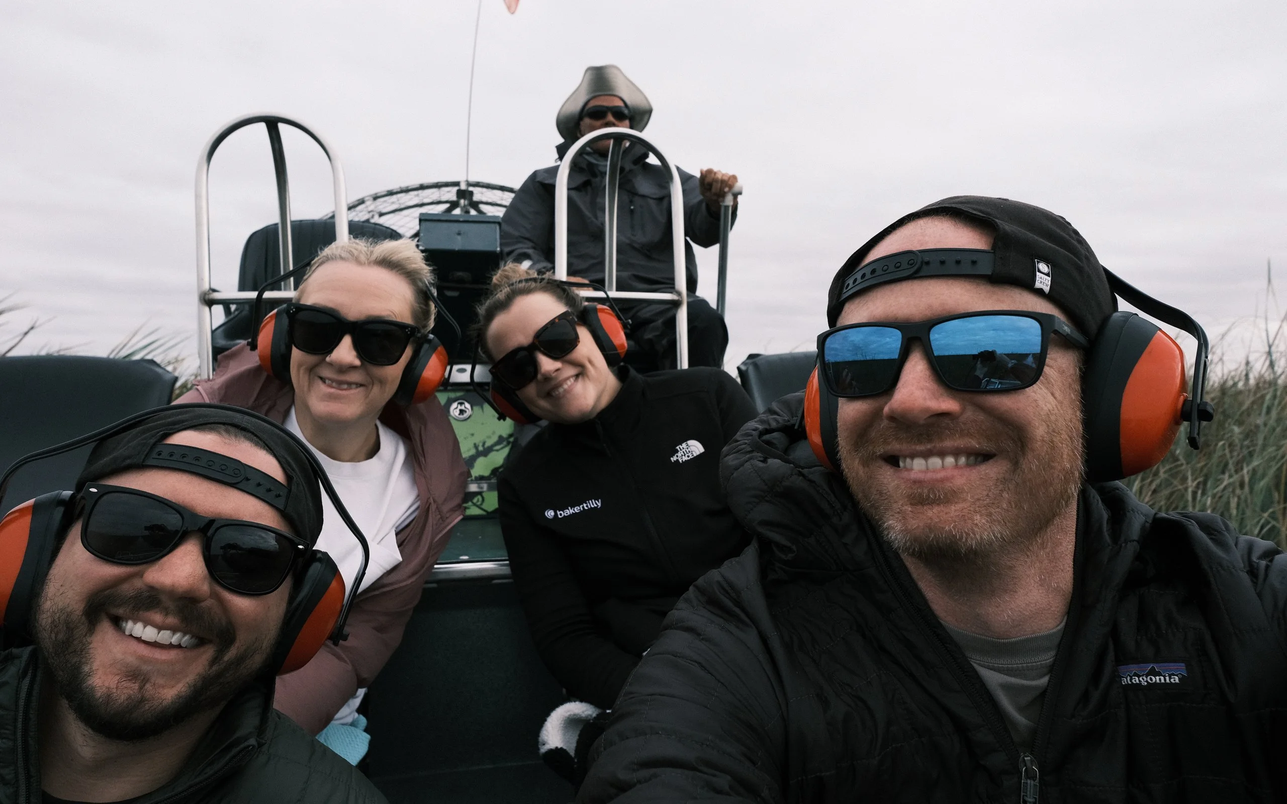 Derek and Josh with friends from Baker Tilly, grinning in ear protection on an airboat