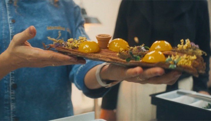 A chef presents a wooden board of plated mango dishes