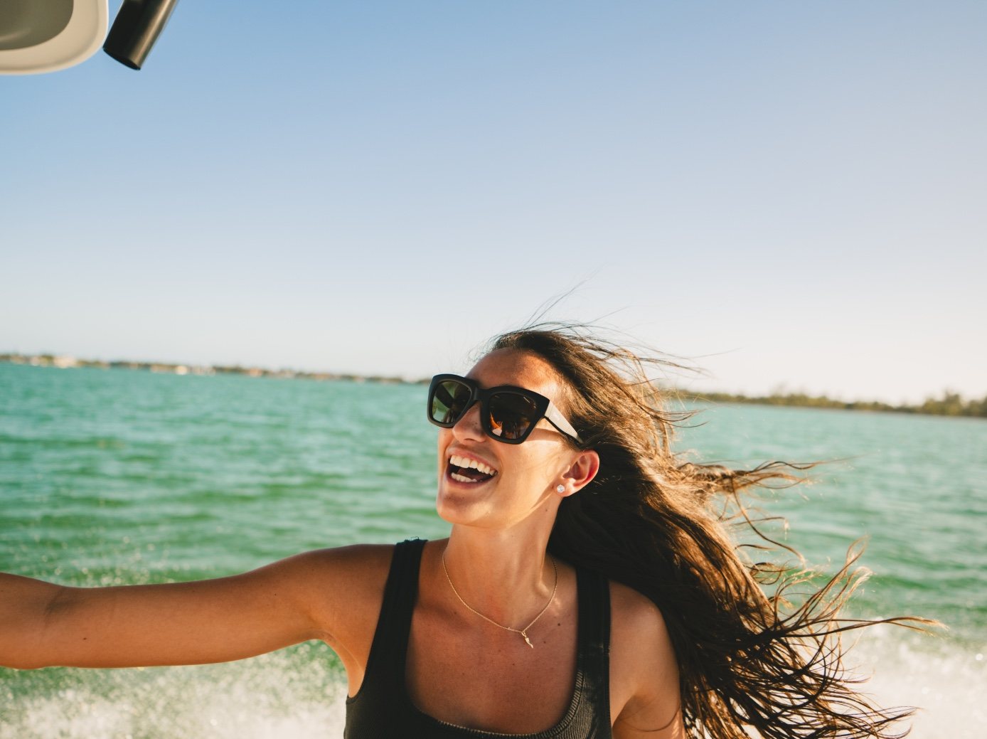 A woman in SMITH sunglasses laughs as the wind whips her hair on a running boat